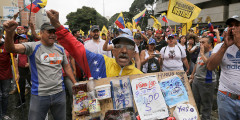 Участник оппозиционнного митинга держит плакат с ценами на продукты. В Венесуэле дефицит продуктов питания и медикаментов. Минимальная зарплата в стране составляет $30 в месяц
