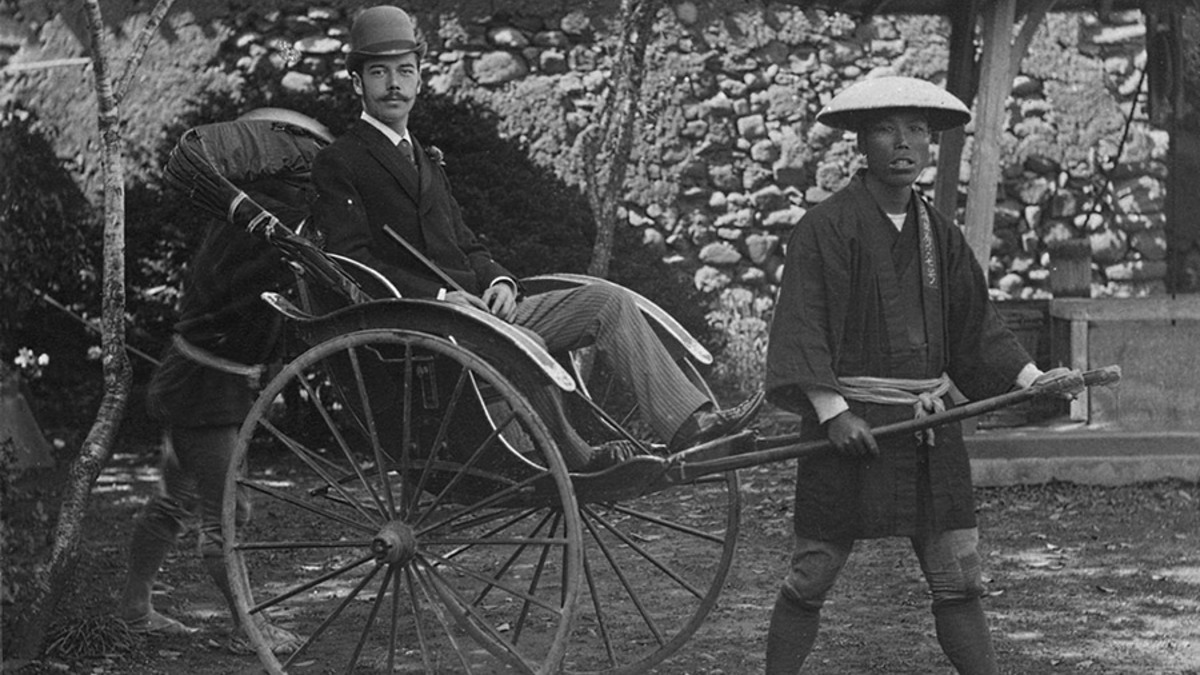 На фото: цесаревич Николай Александрович в Нагасаки, апрель 1891 года.
В октябре 1890 года, после окончания обучения, Николай отправился в длительное путешествие, во время которого посетил Египет, Индию и Японию. В апреле следующего года он был вынужден прервать свою поездку из-за покушения на него в городе Оцу: полицейский внезапно нанес ему удар саблей по голове. Хотя рана оказалась неглубокой и цесаревич быстро поправился, его отец-император настоял на скорейшем возвращении сына.
«Большое путешествие, совершенное им еще наследником, — пишет поэт Георгий Иванов, — поселяет в Николае II ложное представление о необъятности русской мощи на Дальнем Востоке <...>. Здесь, на Дальнем Востоке, цесаревич впервые сознает, кто он такой, какая судьба ему предназначена. В его тихую, бесцветную жизнь впервые врываются сильные ощущения и яркие краски. И, может быть, расположенная к этому, но спавшая до сих пор фантазия впервые «выходит за пределы его огромного царства», когда он <...> слышит звонкие патетические слова: «Россия — предопределенный главарь и покровитель Азии», говорящие о завоеваниях, о военной славе, о гордой, блистательной императорской судьбе».