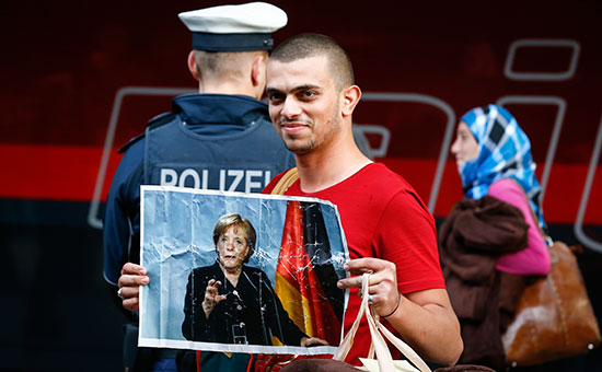 Мигрант держит портрет канцлера Германии Ангелы Меркель после прибытия к главной железнодорожной станции в Мюнхене, Германия