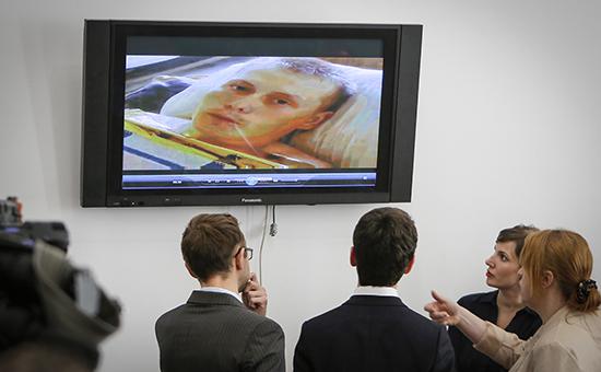 Журналисты смотрят на экран телевизора, по которому показывают допрос российского гражданина Александра Александрова