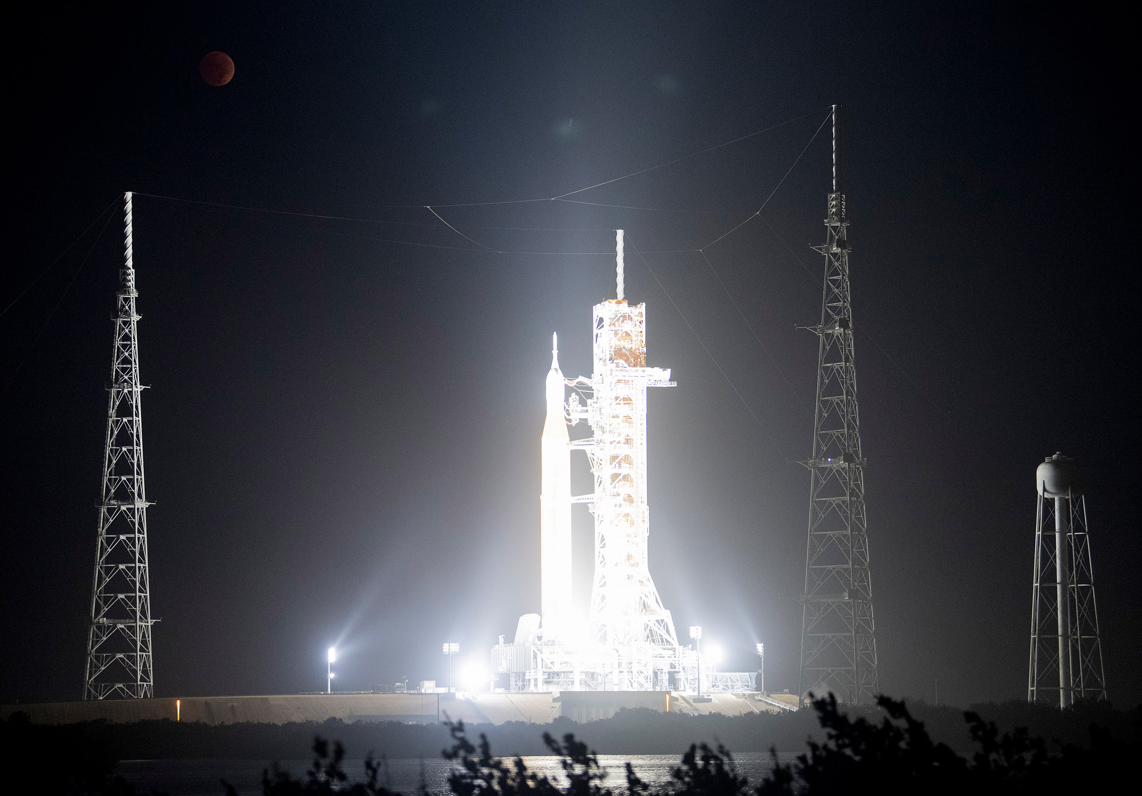 Ракета NASA Space Launch System (SLS) с космическим кораблем Orion на борту мобильной пусковой установки на фоне полного лунного затмения, космический центр Кеннеди НАСА, мыс Канаверал, Флорида