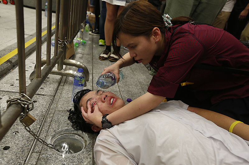 Девушка промывает глаза демонстранту, пострадавшему от воздействия перцового газа.