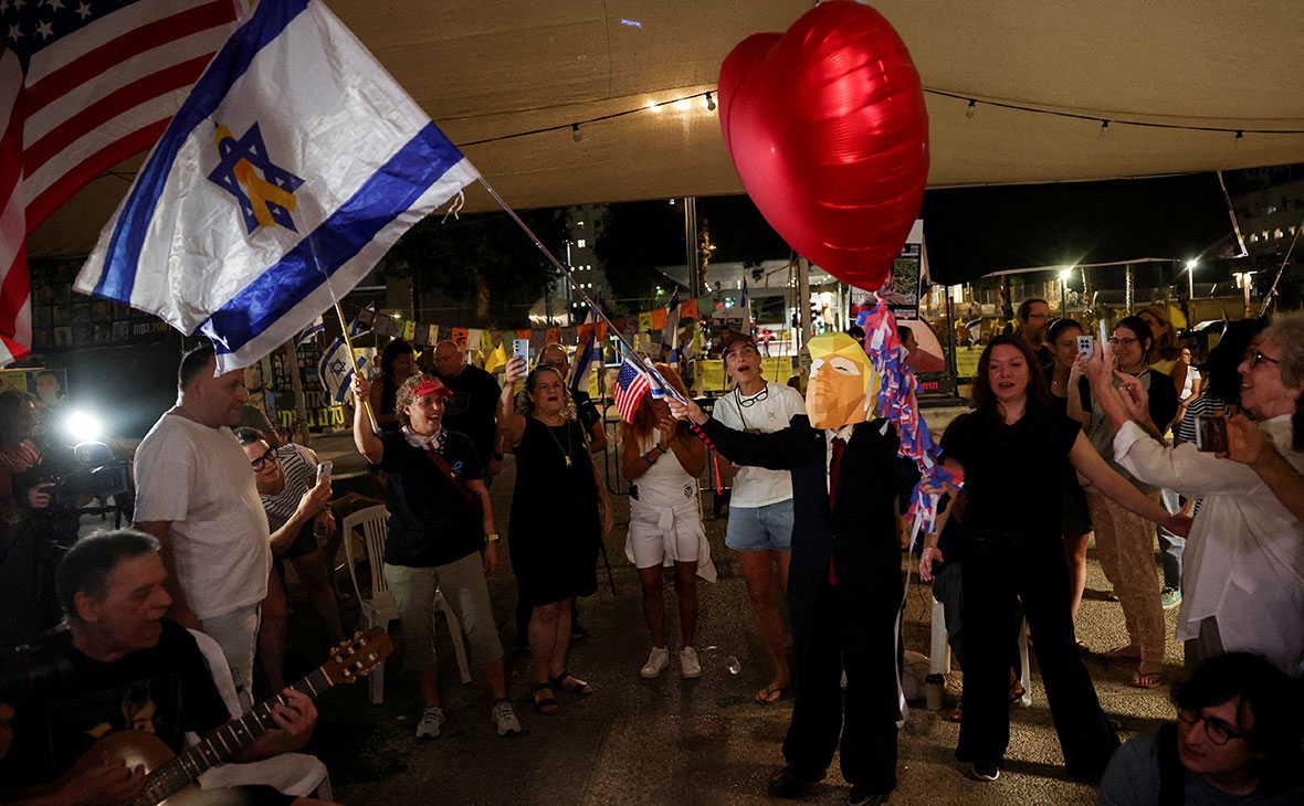 Человек в маске с изображением президента США Дональда Трампа размахивает израильским флагом на «Площади заложников» в Тель-Авиве