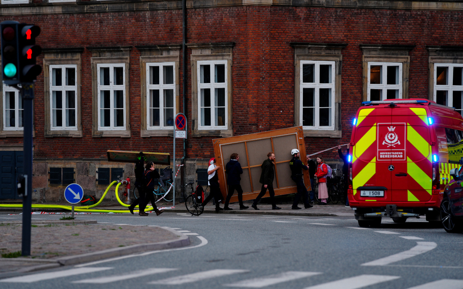 Сотрудник службы спасения помогает людям выносить картины и другие предметы из исторического здания Старой фондовой биржи во время пожара в Копенгагене, Дания, 16 апреля 2024 года