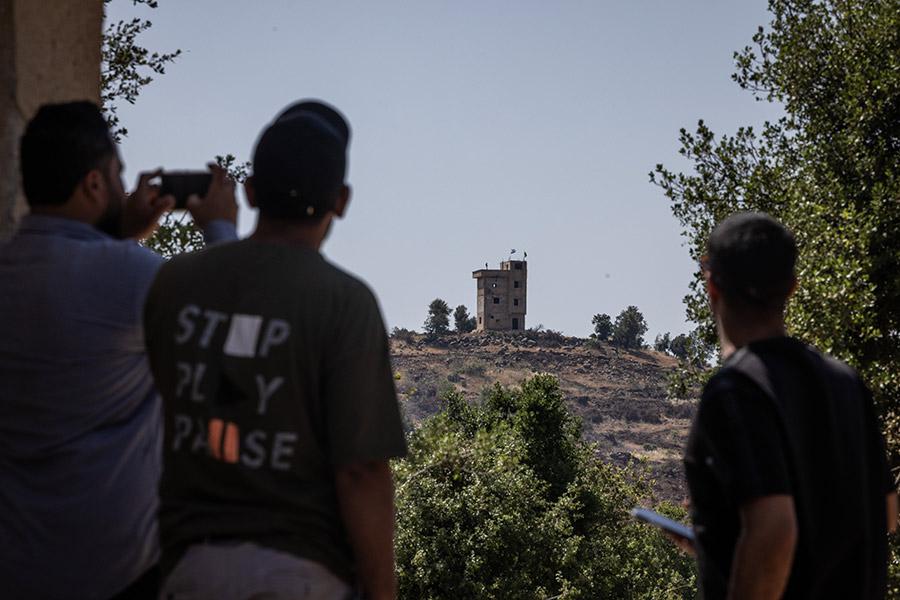 Сирийцы смотрят на здание смотровой площадки с израильским флагом, расположенное на контролируемой Израилем территории, 2025 год