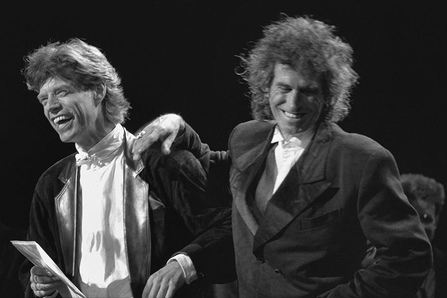 Мик Джаггер и Кит Ричардс смеются во время церемонии награждения в Зале славы рок-н-ролла, где была представлена The Rolling Stones, 18 января 1989 года