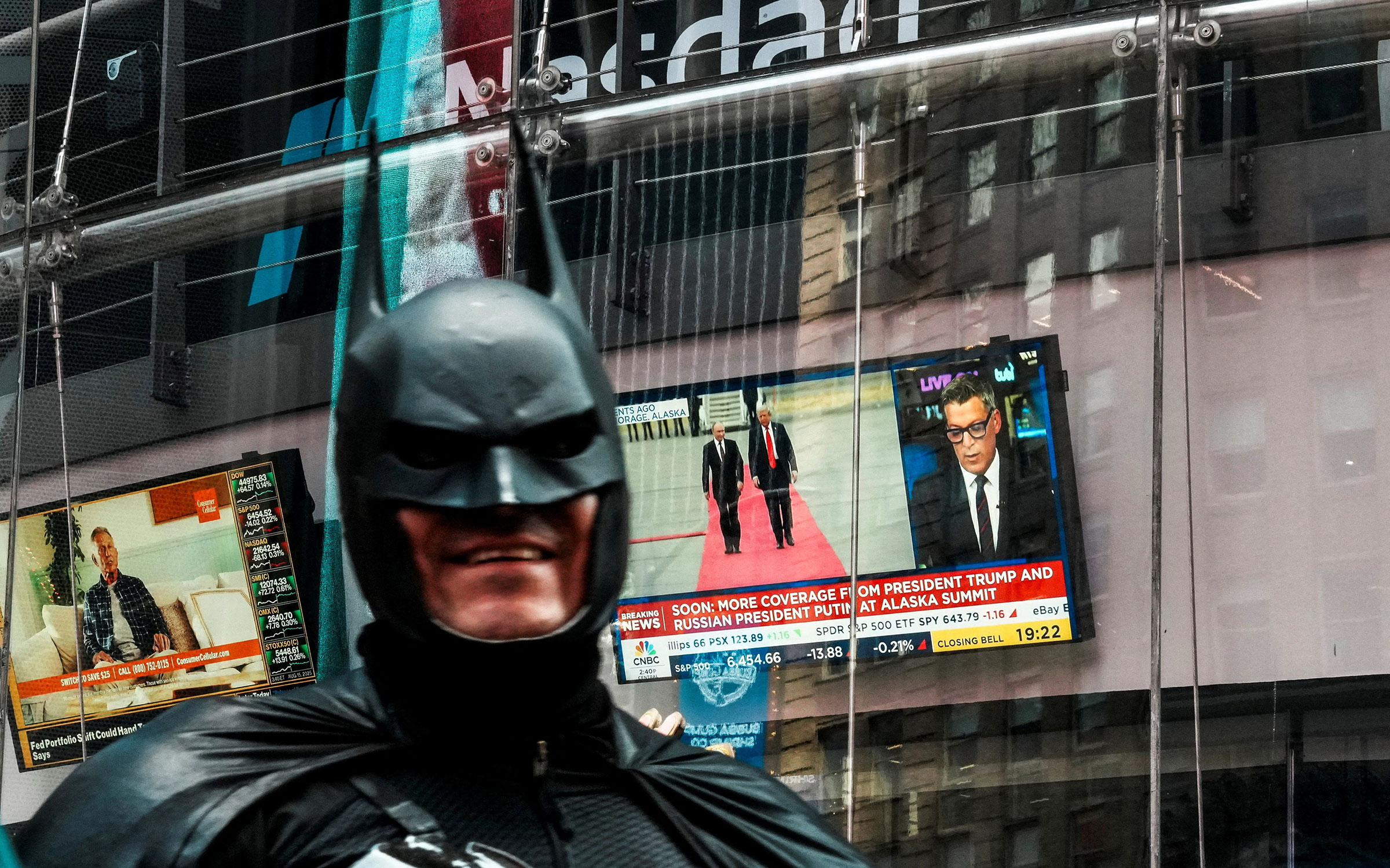 Человек в костюме Бэтмена проходит мимо экрана, на котором показана встреча Дональда Трампа с Владимиром Путиным, на торговой площадке NASDAQ&nbsp;в Нью-Йорке