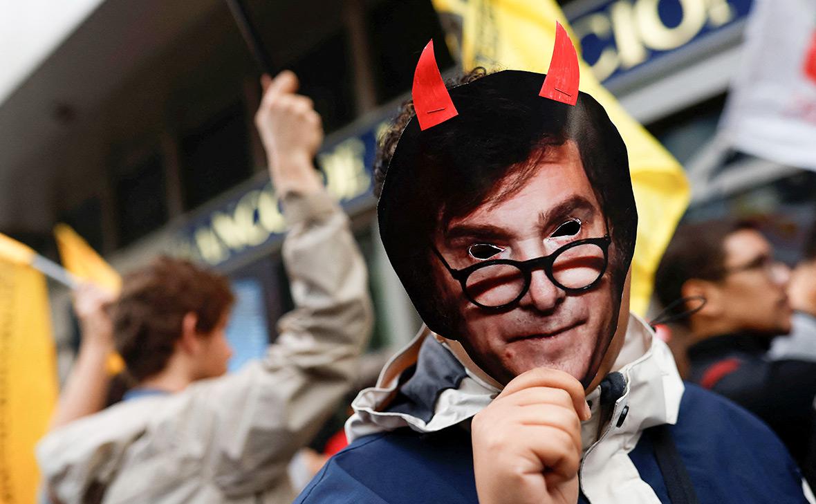 Участник протеста держит маску с изображением Хавьера Милея