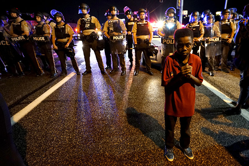 11-летний житель Фергюсона Амарион Аллен стоит перед полицейским оцеплением незадолго до начала стрельбы