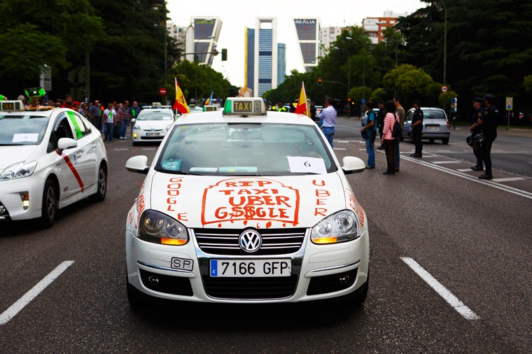 Мадрид, Испания. На фото - один из участников акции, из окон автомобиля которого видны национальные флаги Испании. На капоте такси написано: "RIP Uber такси".