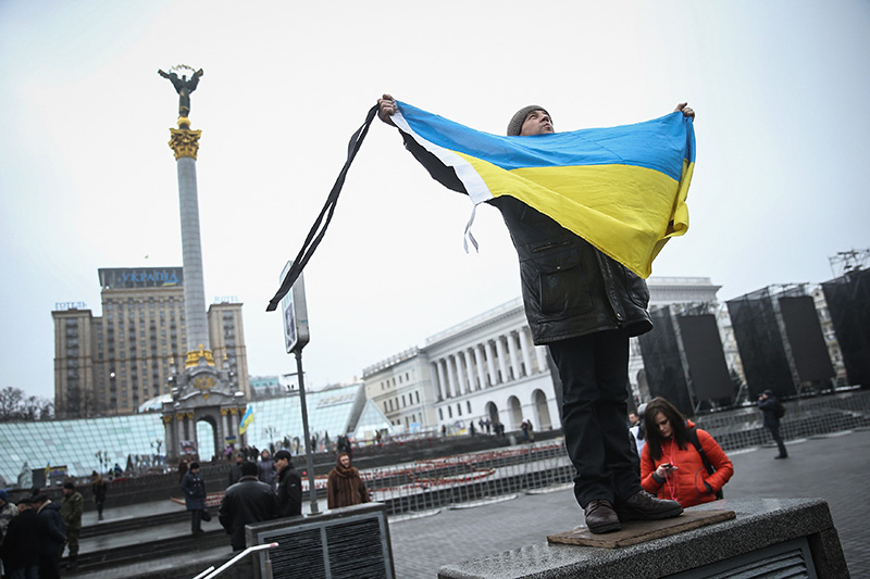 Человек держит флаг Украины с траурными лентами перед началом памятных мероприятий на Майдане
