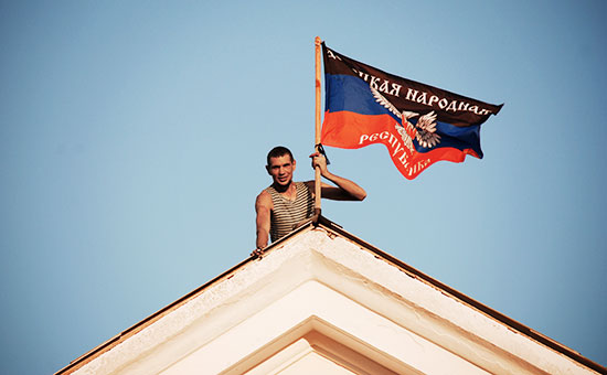 Ополченец Донецкой народной республики (ДНР) устанавливает флаг ДНР на здании мэрии города Комсомольское Донецкой области, сентябрь 2014 г.