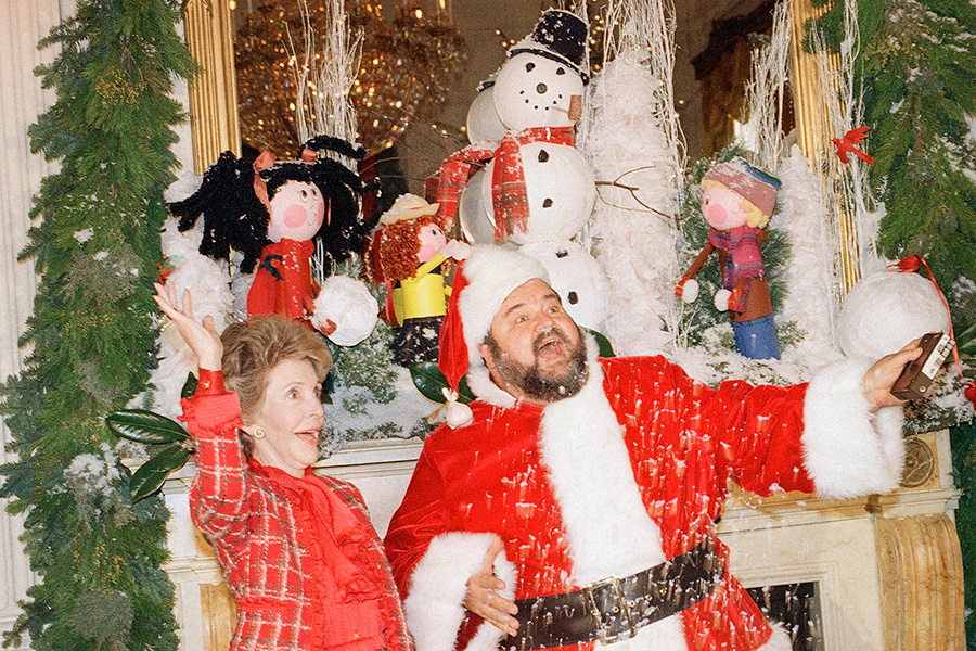 Первая леди Ненси Рейган, жена 40-го президента Рональда Рейгана, и комик Дом Делуиз в костюме Санты, 1987 год. Рождественская ель была &laquo;музыкальной&raquo;, ее украсили миниатюрами в виде инструментов и нотных листов