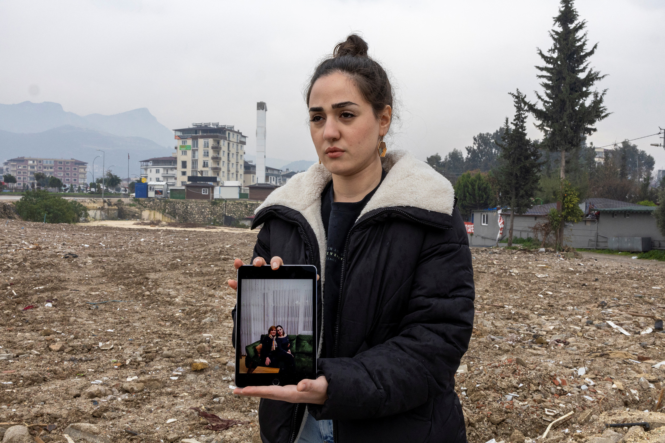 Симге Озгун с фотографией погибшей во время землетрясения матери Ремзие стоит на месте, где был их дом в Хатае, 3 февраля.