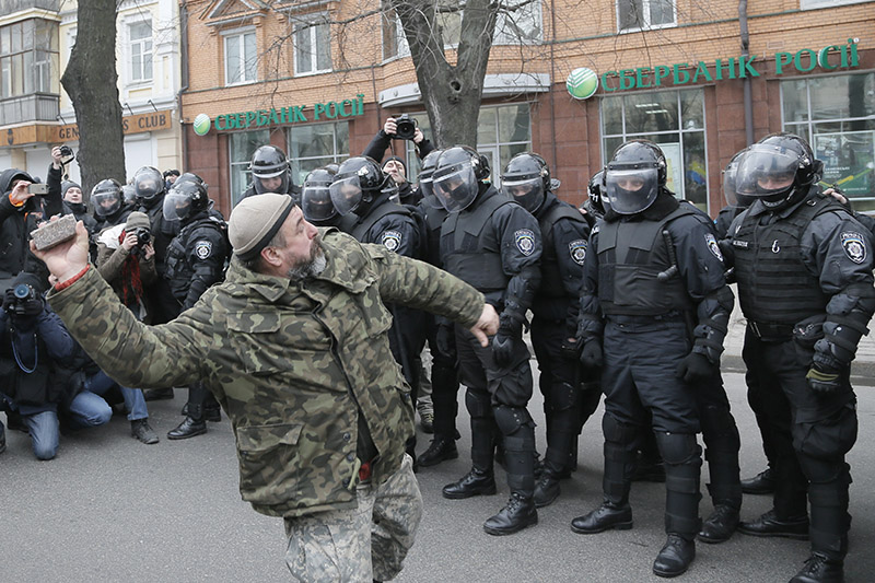 Участник акции протеста швыряет камень в окно отделения Сбербанка. В годовщину Евромайдана&nbsp;в Киеве устроили погромы в нескольких отделениях российских банков
