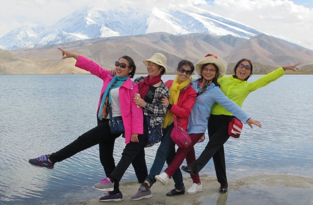 Китайские туристы на берегу озера Каракёль позируют на фоне горы Музтагата в западном Китае