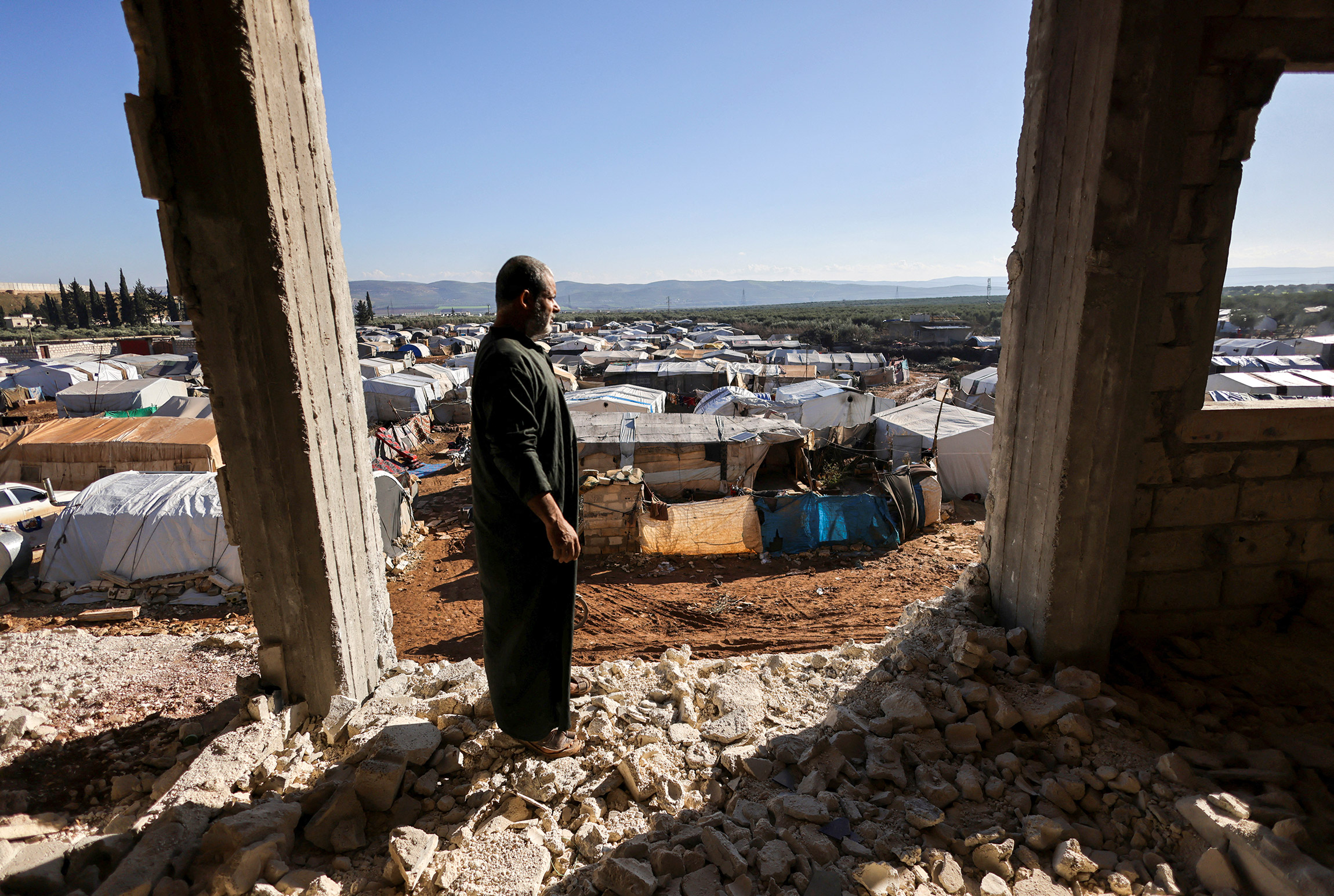 Выживший во время землетрясения Амер Халил стоит в разрушенном здании, где была его квартира. Рядом стоит палаточный городок, где сейчас живет мужчина. Город Джандарис (Сирия), 24 января.