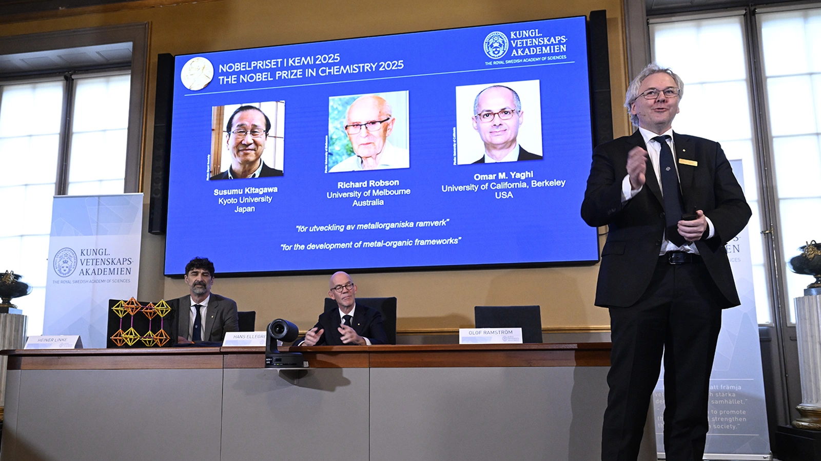 Церемония объявления лауреатов Нобелевской премии 2025 года по химии, которыми стали (на экране на дальнем плане): Сусуму Китагава (США), Ричард Робсон (Австралия) и Омар Яги (США)