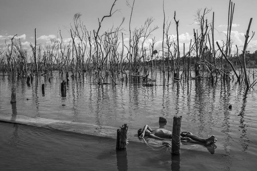 На фото:  мальчик отдыхает на мертвом стволе дерева на реке Шингу в Паратизау&nbsp;&mdash; поселке недалеко от ГЭС Белу-Монти, 28 августа 2018 года. Позади&nbsp;&mdash; деревья, омертвевшие после затопления водохранилища