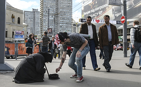 Молодой человек бросает мелочь женщине, собирающей милостыню на улице Новый Арбат