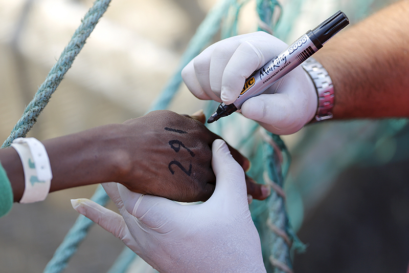Сотрудник миграционной службы пишет идентификационный номер на руке нелегала, добравшегося на лодке до итальянского города Катания


