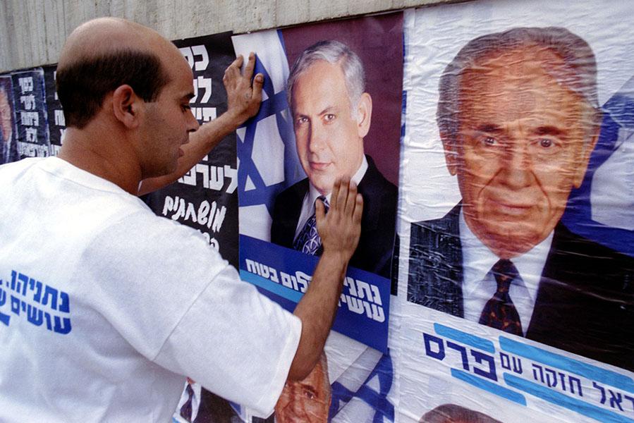 Активист партии &laquo;Ликуд&raquo; наклеивает плакаты с изображением Биньямина Нетаньяху&nbsp;поверх предвыборных плакатов премьер-министра Шимона Переса