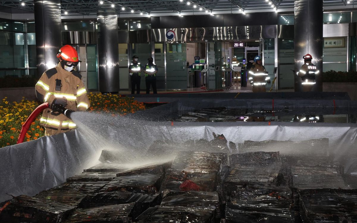 Пожарный обливает водой сгоревшие литий-ионные аккумуляторы после пожара в NIRS