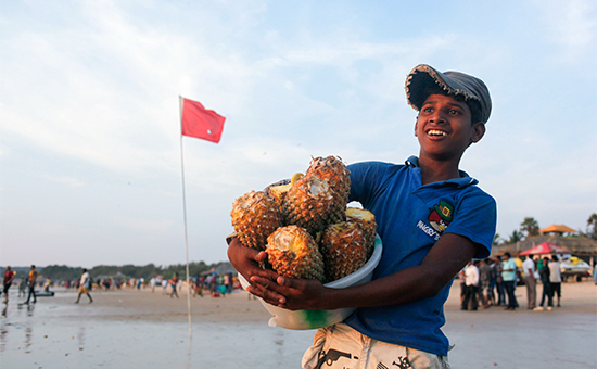 Индийский мальчик продает ананасы на пляже Калангут, Гоа