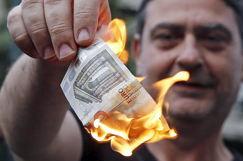 Протестующий поджигает банкноту евро во&nbsp;время демонстрации около офиса ЕС&nbsp;в Афинах
