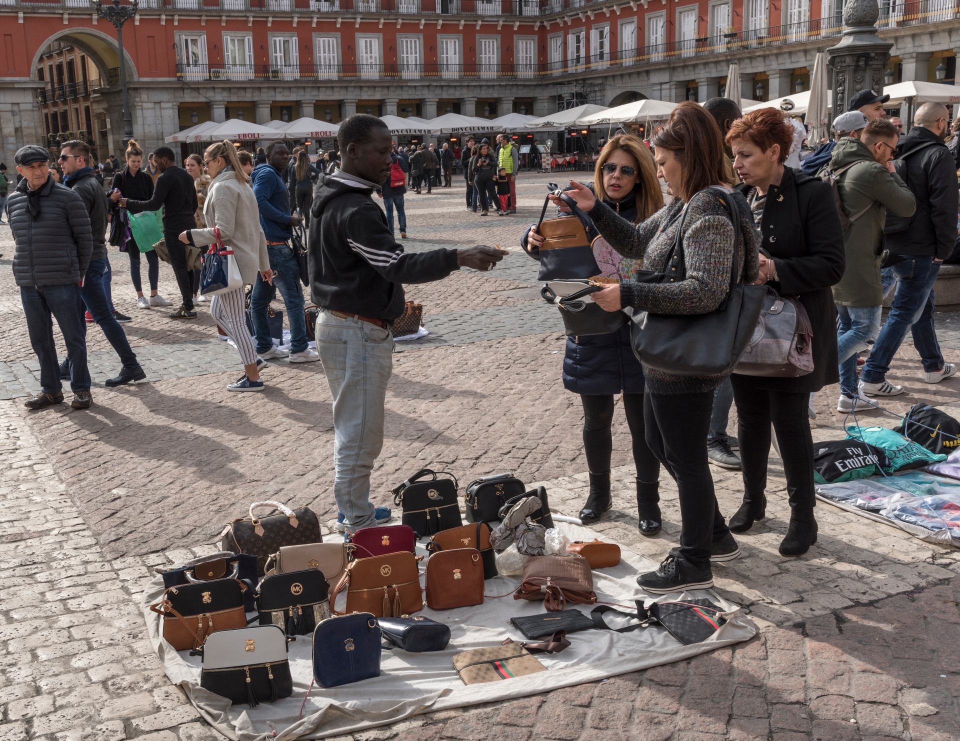 Туристы разглядывают поддельные сумки Tous и Michael Kors