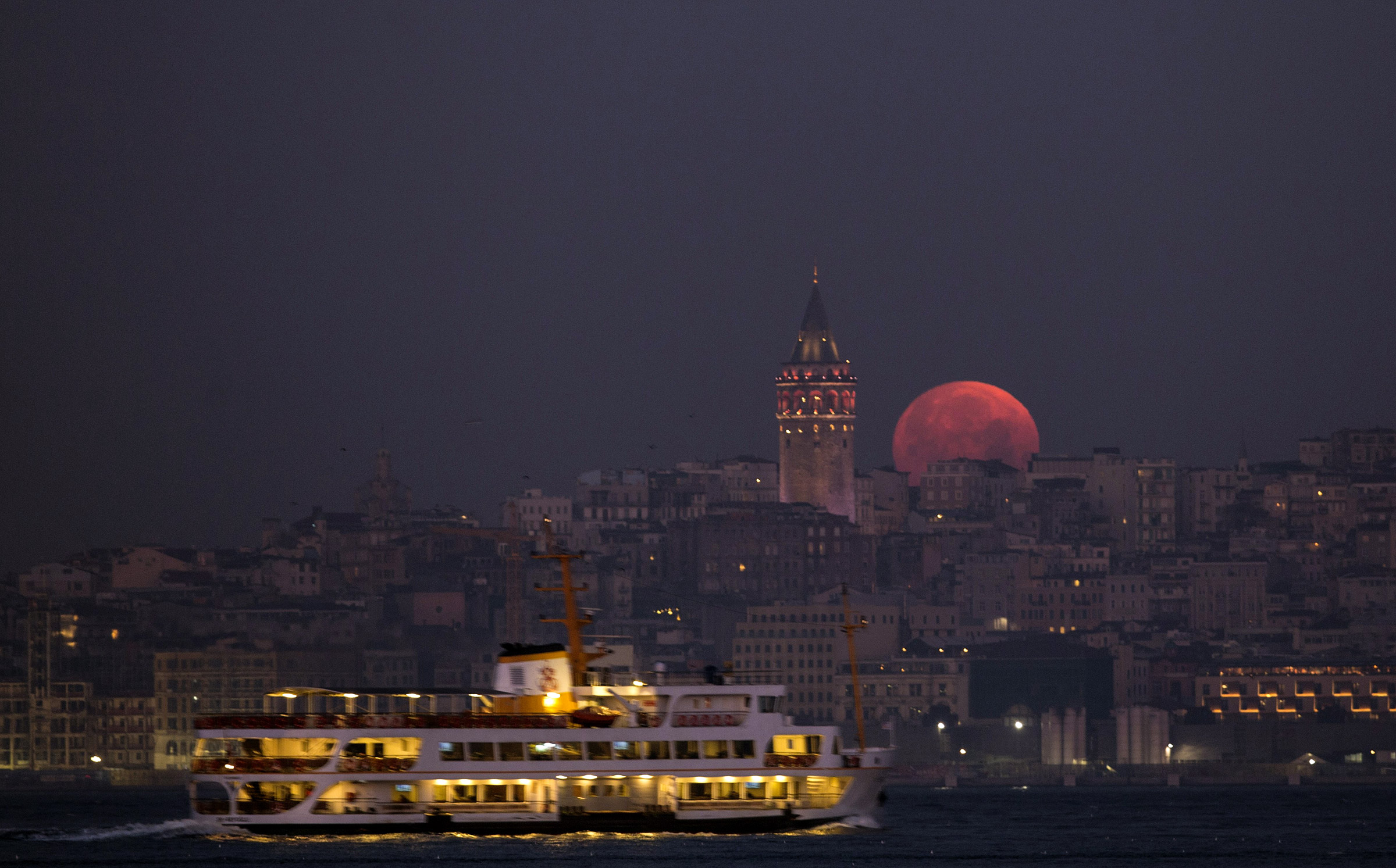 Луна поднимается в небо рядом с Галатской башней, возвышающейся над европейской частью Стамбула.
