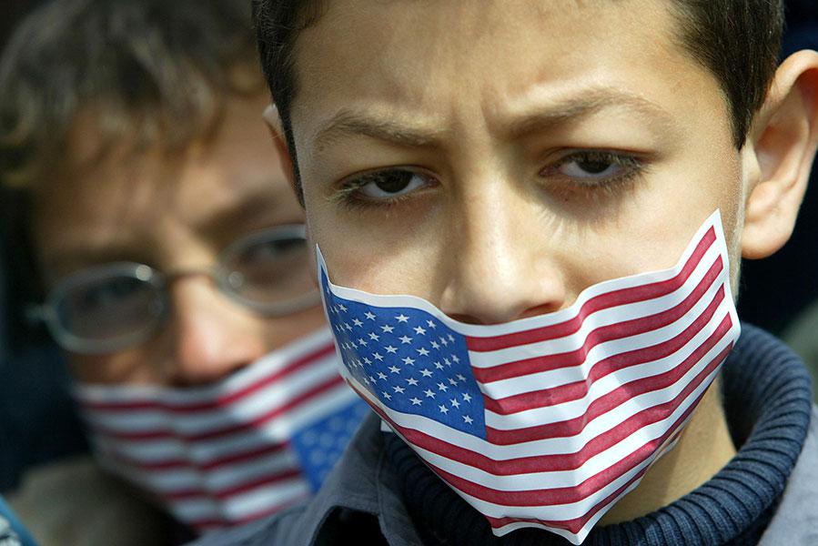 Палестинские мальчики заклеивают рты наклейками с американским флагом во время антиамериканского митинга в лагере беженцев Рафах в секторе Газа, 20 марта 2003 года. Крылатые ракеты «Томагавк» были выпущены по иракским объектам рано утром 20 марта