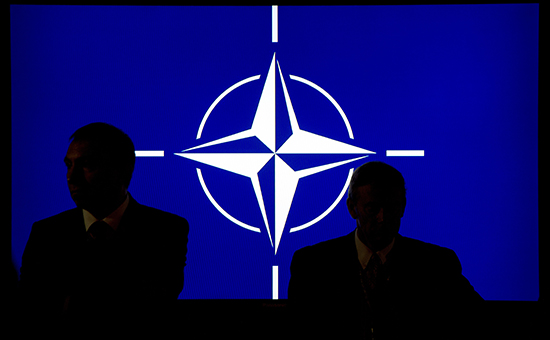 Люди на&nbsp;фоне логотипа НАТО


