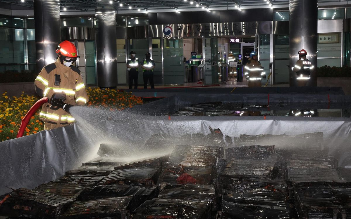 Пожарный обливает водой сгоревшие литий-ионные аккумуляторы после пожара в NIRS