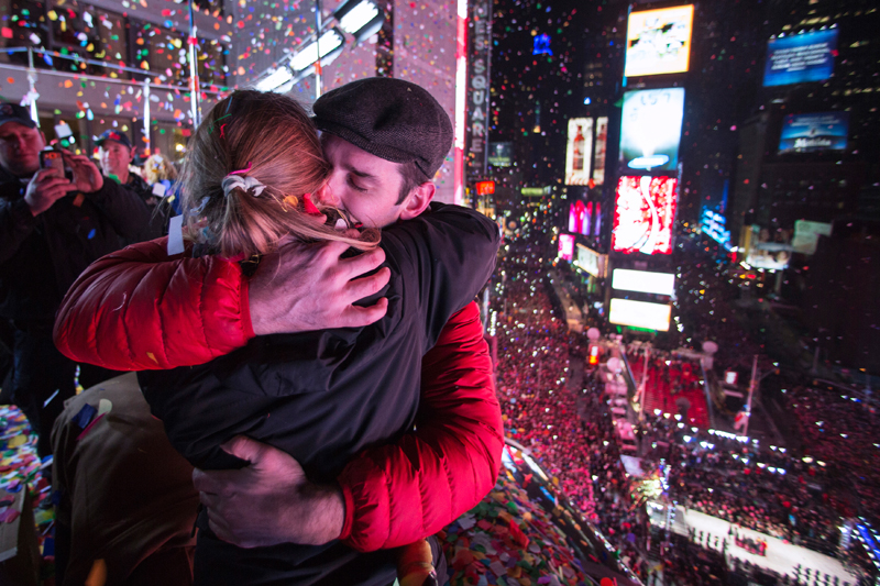 Пара обнимается на балконе на Таймс-сквер в Нью-Йорке. Часы только&nbsp;что пробили полночь, и в воздухе летает конфетти.