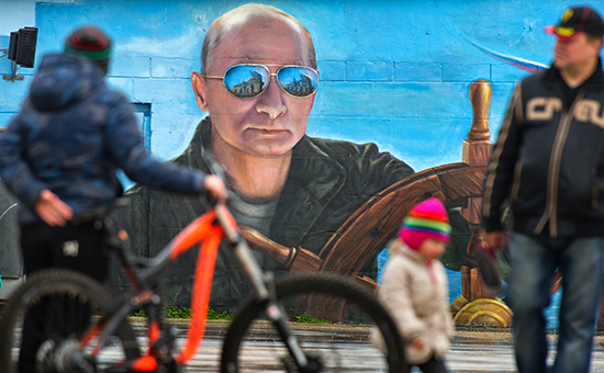 Прохожие у портрета президента России Владимира Путина на стене здания


