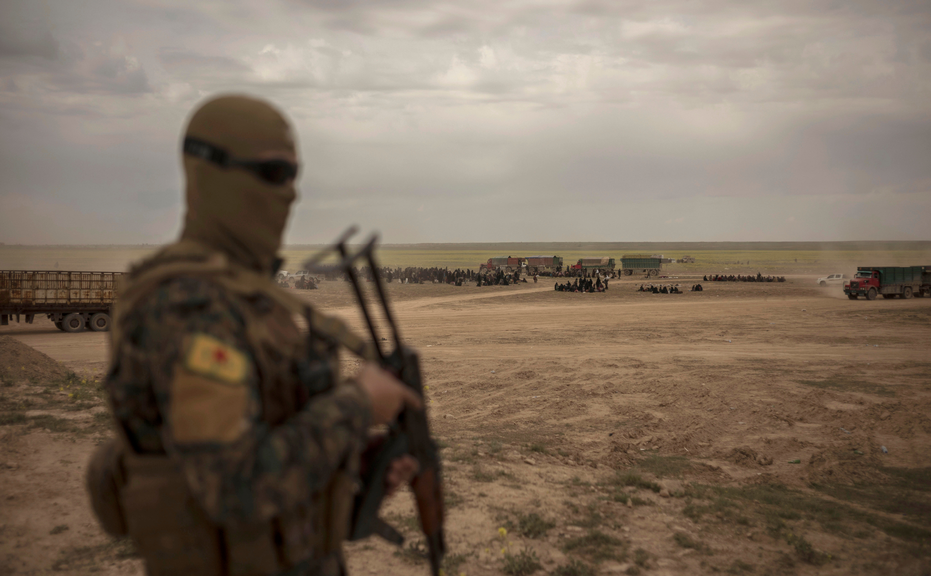 Член SDF на фоне колонны людей, эвакуирующихся из Багуза