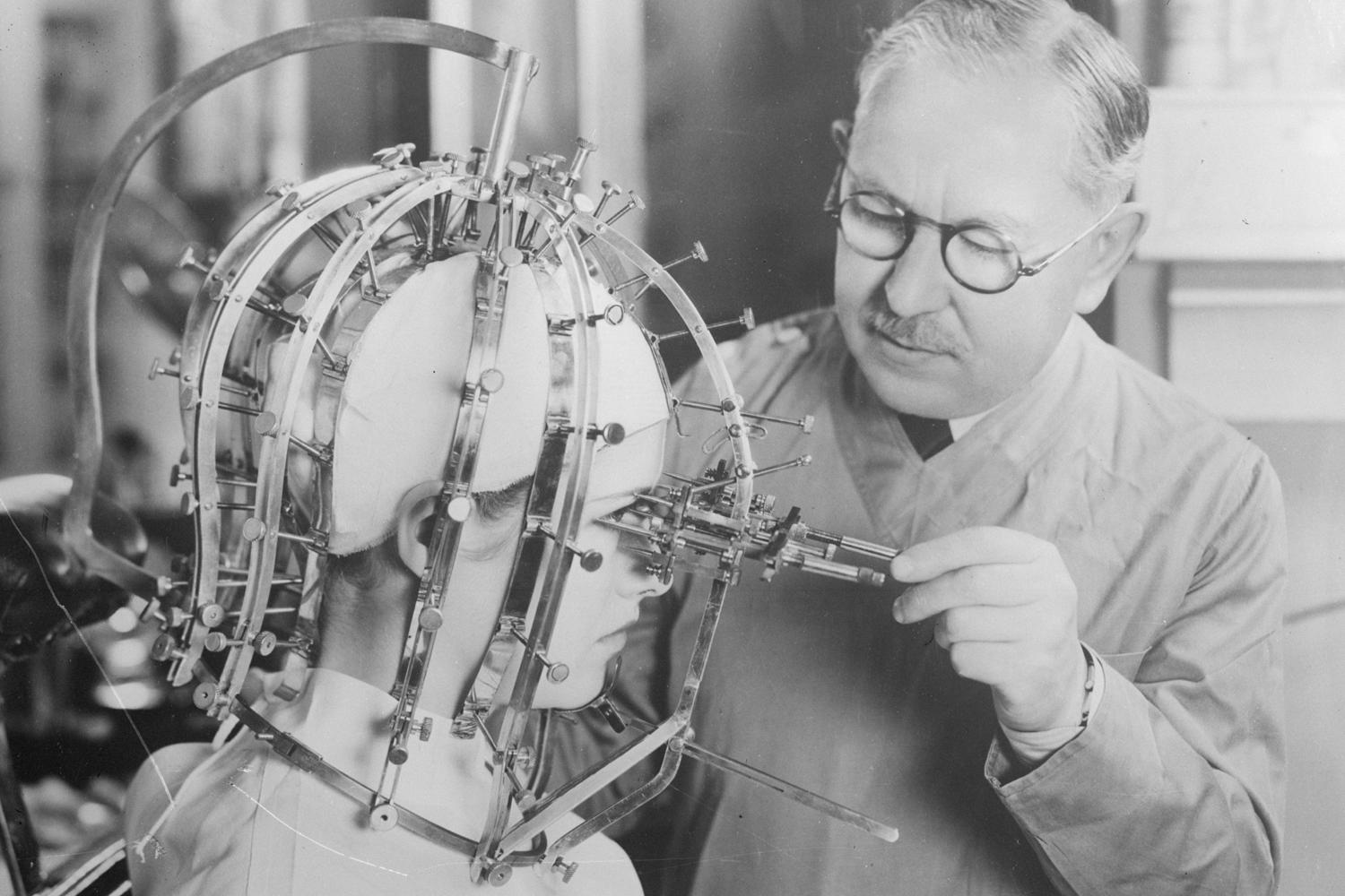 Макс Фактор проводит точные измерения головы и лица молодой женщины с помощью устройства &laquo;Калибратор красоты&raquo;, примерно 1933 год