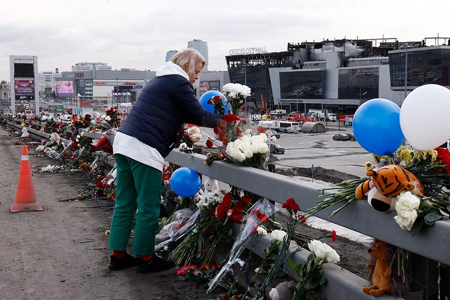 Цветы в память о погибших при теракте на фоне сгоревшего здания концертного зала &laquo;Крокус сити холл&raquo;, Красногорск, Московская область, 2024 год