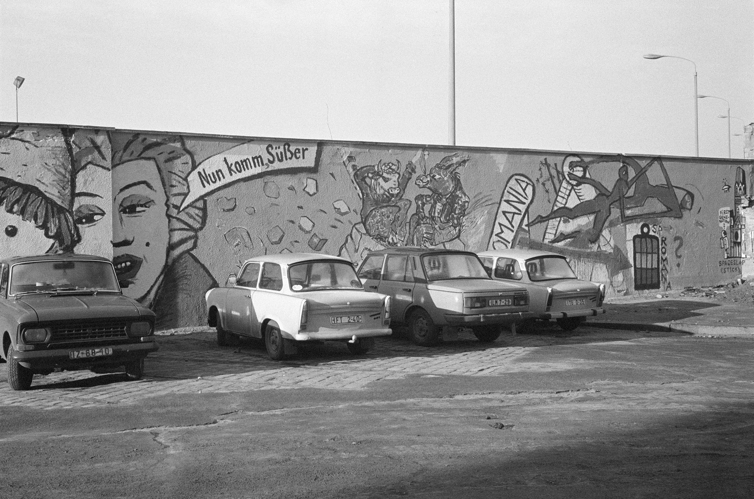 На фото: парковка в ГДР с автомобилями Wartburg 353 и Trabant, 26 декабря 1989 года.

Trabant производился с ноября 1957 по апрель 1991 и был назван в честь советского спутника, который запустили за месяц до старта производства. Несмотря на высокопарное название, в простонародье автомобиль называли &laquo;гоночной картонкой&raquo;, &laquo;пластиковым бомбардировщиком&raquo; и &laquo;местью Хонеккера&raquo; (генсека&nbsp;социалистической партии ГДР). Из-за низкой цены это был самый распространенный автомобиль в ГДР, всего за 34 года было произведено около 3,7 млн машин. Однако в очереди на его покупку можно было простоять более десятилетия, из-за чего даже появилась шутка: &laquo;Почему в ГДР не грабят банки? Потому что машину после ограбления нужно было&nbsp;бы ждать 12 лет!&raquo;

Wartburg 353 начали производиться в 1966 году. Помимо соцблока, его экспортировали в Бельгию, Финляндию, Великобританию и даже ЮАР, несмотря на то, что &laquo;зазоры между панелями кузова с одной стороны вполне могли отличаться от зазоров с другой на толщину пальца&raquo;. К 1991 году, когда производство было остановлено, было выпущено более 1,2 млн Wartburg 353 и 353W.