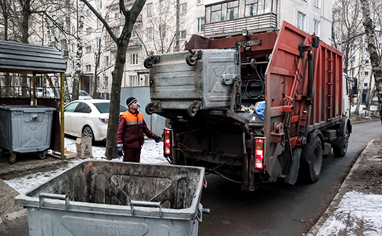 Сотрудник коммунальных служб выгружает мусор из контейнера в мусоровоз.