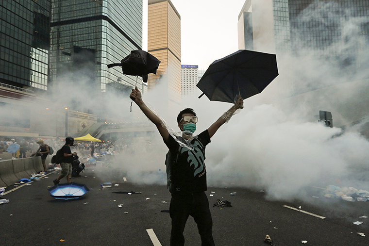 При разгоне демонстрантов, заблокировавших финансовый центр Гонконга, полиция применила слезоточивый газ.&nbsp;Протестующие прикрываются зонтами.