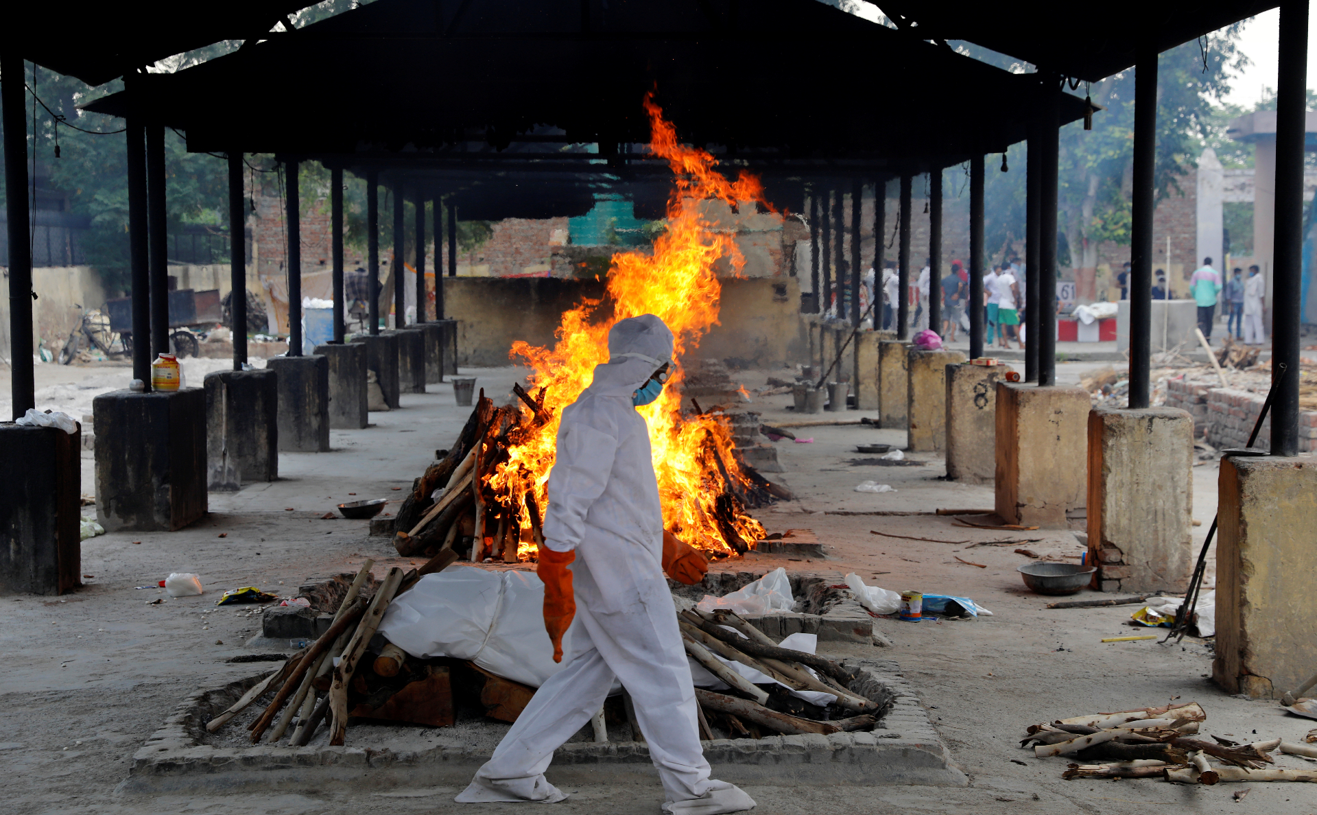 Священник, одетый в защитный костюм, проходит рядом с погребальным костром, приготовленным для сжигания тела умершего от COVID-19. Нью-Дели, Индия