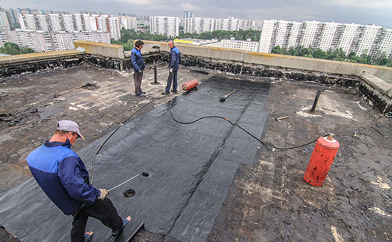 Укладка нового рубероида на крыше во время капитального ремонта многоэтажного панельного дома