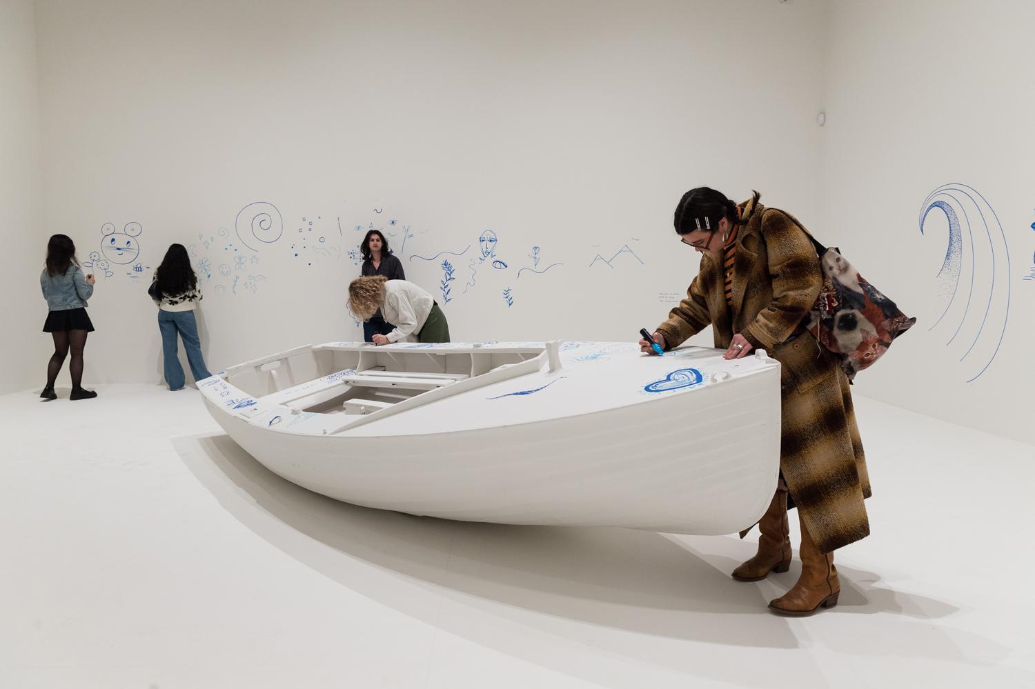 Посетитель раскрашивает лодку на превью выставки &laquo;Yoko Ono: Music Of The Mind&raquo; в галерее Tate Modern, Лондон, Великобритания, 2024. Проект &laquo;Add Color (Refugee Boat)&raquo; (идея&nbsp;&mdash; 1960, первая воплощение&nbsp;&mdash; 2016)
