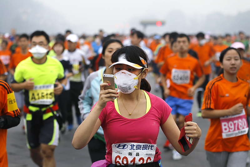 Участница марафона в маске и смартфоном в руке.