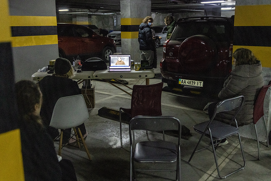 Жители Киева смотрят новости на парковке многоквартирного дома, использующейся как бомбоубежище