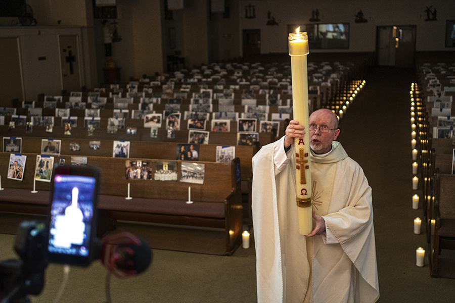 Пастор Николас Санчес несет пасхальную свечу в церкви в Северном Голливуде, Калифорния. Скамьи украшены фотографиями, которые прислали прихожане
