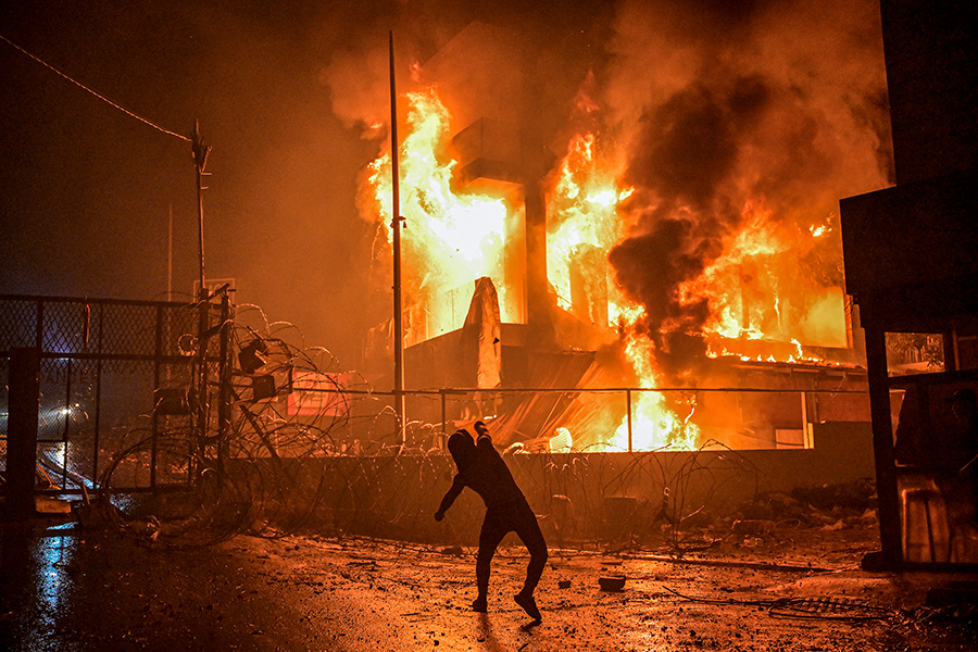 Протестующий в Бейруте (Ливан) кидает камни в сторону горящего здания у посольства США.