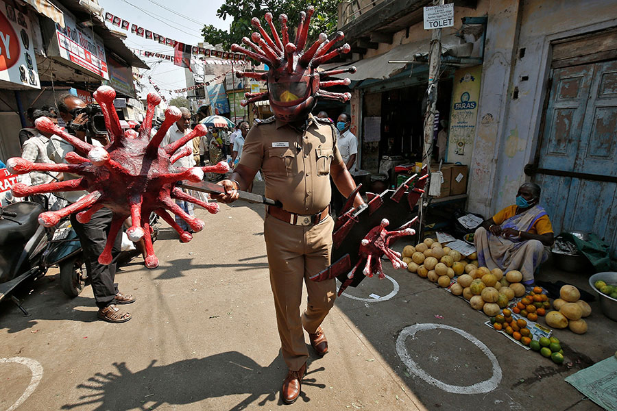 Офицер полиции в шлеме, изображающем коронавирус, оповещает людей на рынке о необходимости соблюдать безопасную дистанцию. Ченнай, Индия
